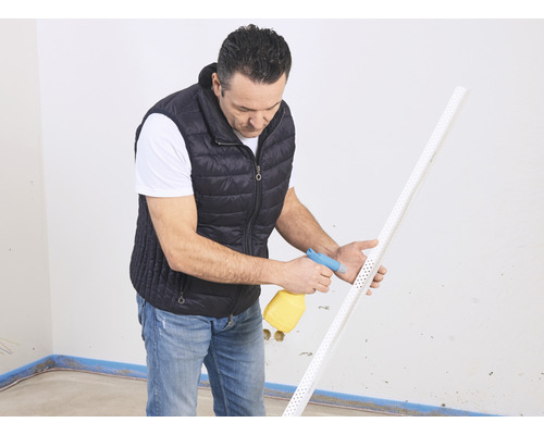 Ein Mann befeuchtet ein Putzprofil mit einer Sprühflasche in einem Raum.