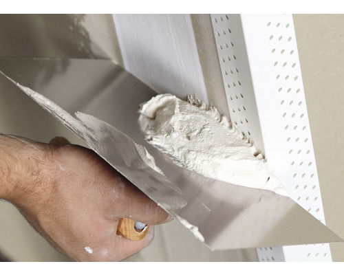 Handwerker trägt mit einer Spachtel Putz auf eine Wand auf.