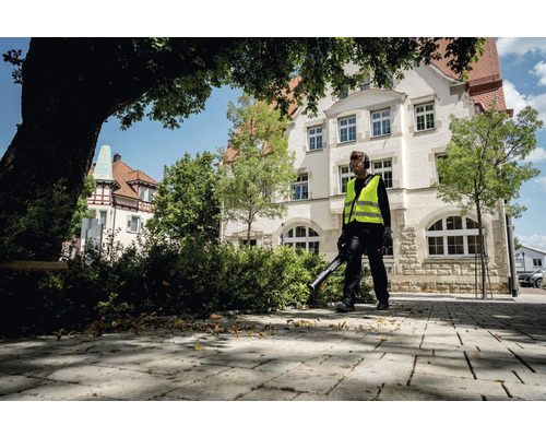Un homme avec un souffleur de feuilles nettoie le trottoir devant un bâtiment