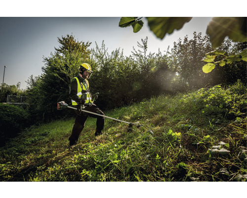 Une personne portant un équipement de sécurité utilise une débroussailleuse pour couper l''herbe