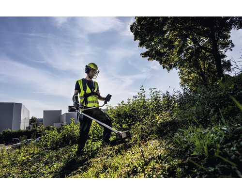 Un homme travaille avec un coupe-bordure dans un champ, portant des vêtements de protection.