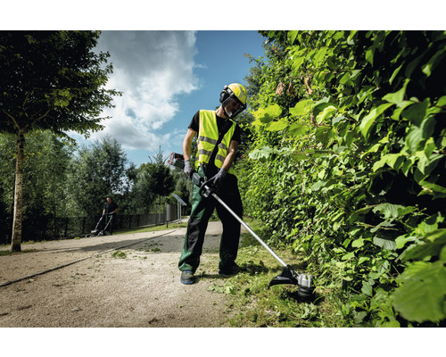 Une personne coupe une haie dans le jardin avec une débroussailleuse.