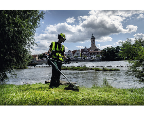 Une personne coupe l''herbe avec un coupe-bordure près d''une rivière.