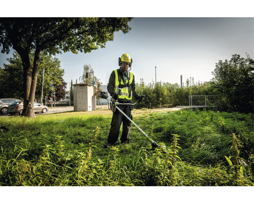 Un homme coupe de l''herbe haute avec un coupe-bordure dans un environnement urbain.