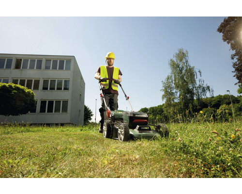 Un homme tond le gazon avec une tondeuse Metabo dans le jardin.