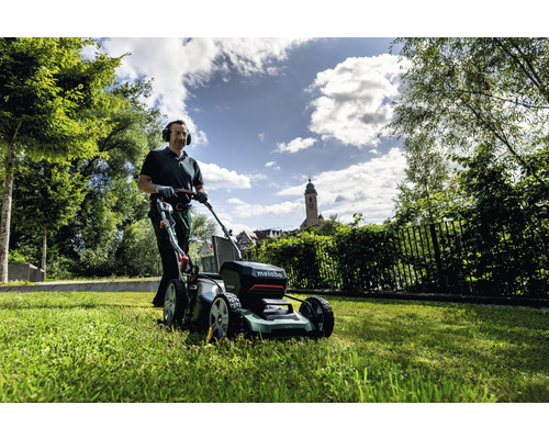 Un homme tond la pelouse avec une tondeuse à gazon sans fil Metabo dans le jardin.