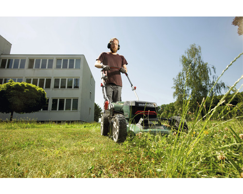 Un homme portant une protection auditive tond la pelouse avec une tondeuse à gazon Metabo
