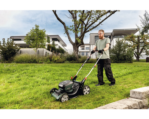 Un homme tond la pelouse avec une tondeuse à gazon à batterie dans un jardin.