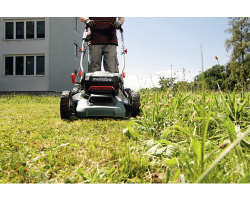 Un homme utilise une tondeuse à gazon sur une pelouse. Logo Metabo.