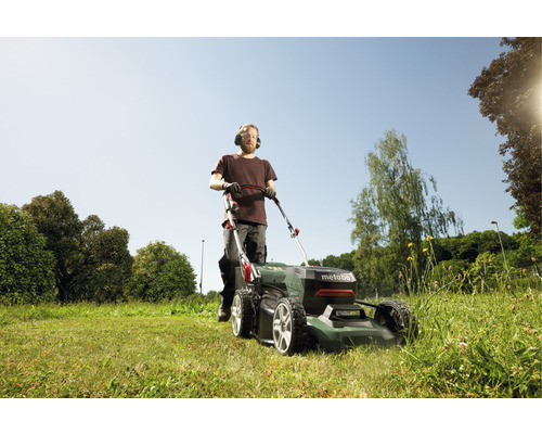Un homme tond la pelouse avec une tondeuse à gazon Metabo dans le jardin.
