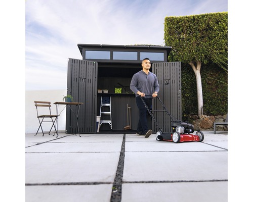 Scène avec une tondeuse à gazon devant un abri de jardin ouvert, une échelle et des meubles de jardin