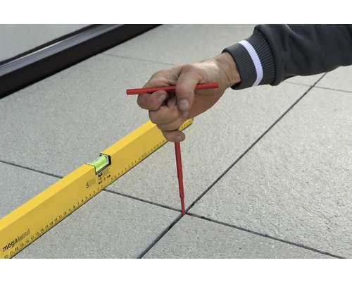 Une personne marque les joints entre les dalles de terrasse avec une croix à joint et un niveau à bulle.