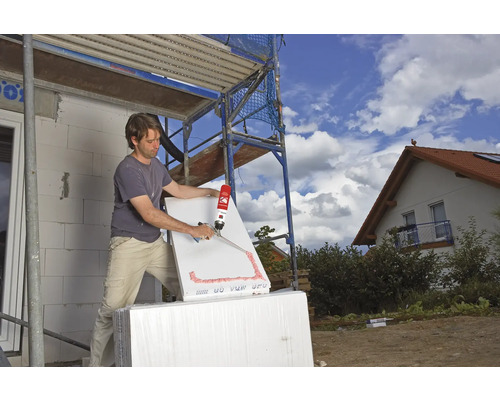 Ein Mann verwendet Bauschaum auf einer Dämmplatte auf einer Baustelle.
