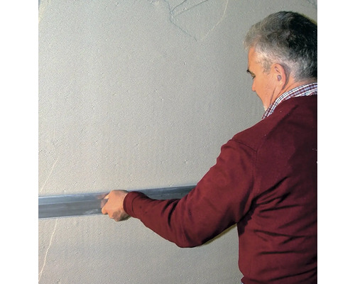 Un homme lisse un mur avec une règle à araser