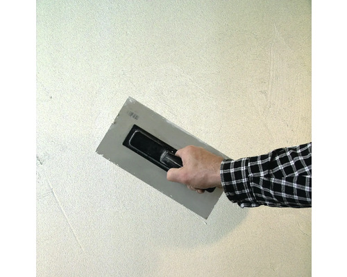 Artisan lissant du plâtre avec une taloche sur un mur.