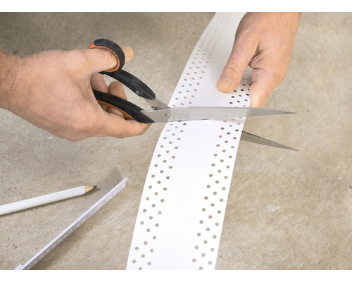 Une personne coupe un profilé de protection des bords perforé avec des ciseaux.