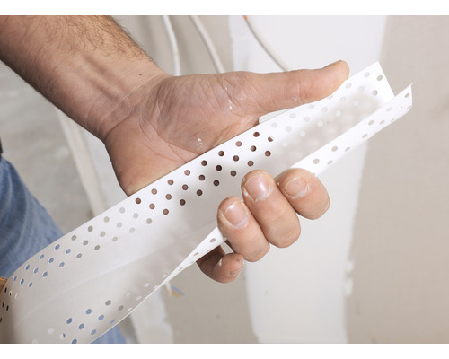 Une main tient un profilé de protection d''angle perforé pour cloisons sèches.