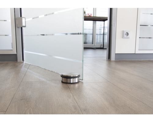 Butoir de porte en acier inoxydable sur plancher en bois devant une porte en verre