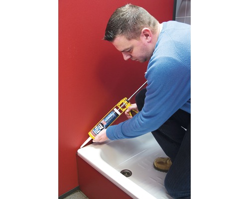 Une personne étanchéifie une baignoire avec un pistolet à cartouche et du mastic.
