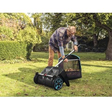 Un homme utilise une balayeuse à gazon dans le jardin pour ramasser les feuilles.