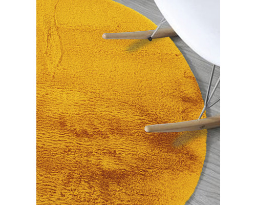 Detailansicht eines runden, zotteligen Teppichs neben einem Stuhl