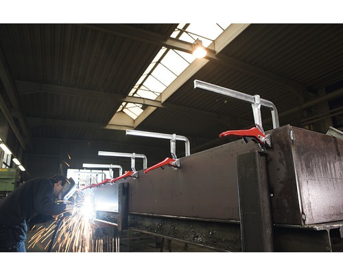 Un ouvrier soude du métal avec des serre-joints dans un atelier.