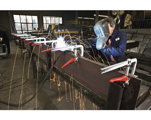 Un homme soude du métal avec un serre-joint dans un atelier.