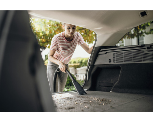 Une femme aspire le coffre d''une voiture avec un aspirateur