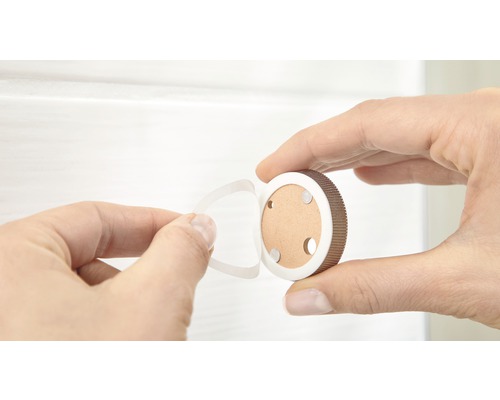 Une main tient un support de verrou magnétique rond et retire le film protecteur de la pastille adhésive.