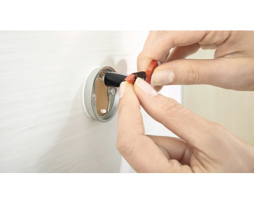 Une personne insérant un conducteur électrique dans une boîte de connexion murale