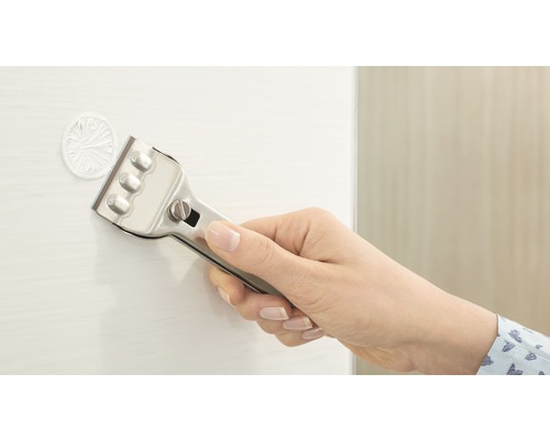 Main avec grattoir à verre enlevant un autocollant d''une surface