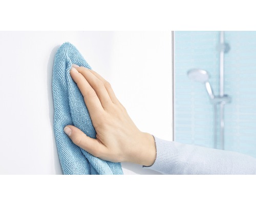 Une main essuie une surface blanche avec un chiffon de nettoyage dans une salle de bain.