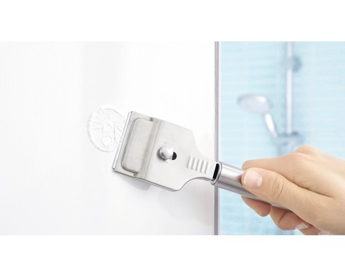 Une main utilise un grattoir à vitre pour enlever des autocollants dans une salle de bain.