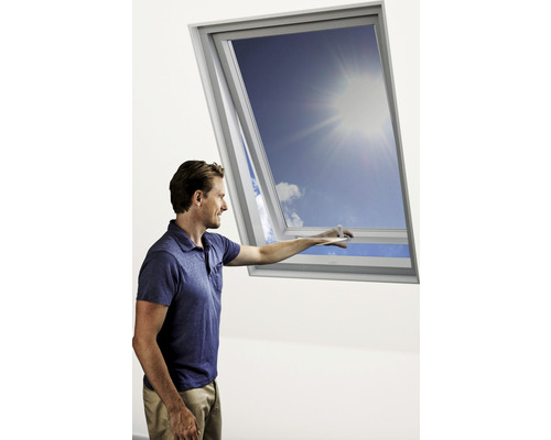 Un homme ouvre une fenêtre de toit et regarde le ciel bleu.