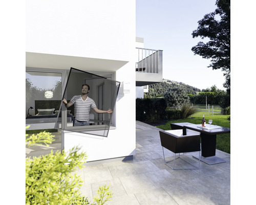 Mann montiert Insektenschutzgitter vor einem Fenster eines Hauses mit Terrasse