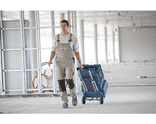 Artisan tirant une boîte à outils à roulettes de Bosch à travers une coquille brute.