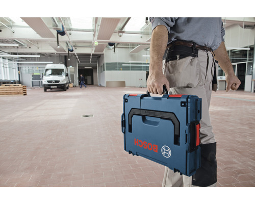 Un artisan transporte une boîte à outils de la marque Bosch dans un entrepôt.