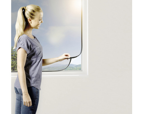 Eine Frau befestigt ein Insektenschutzgitter an einem Fenster.