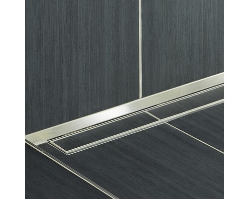 Gros plan d''un siphon de douche en métal dans une salle de bains avec des carreaux foncés.