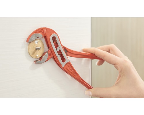 Eine Person benutzt eine Rohrzange, um einen Holzdübel mit Schraube in eine weisse Oberfläche zu drehen.