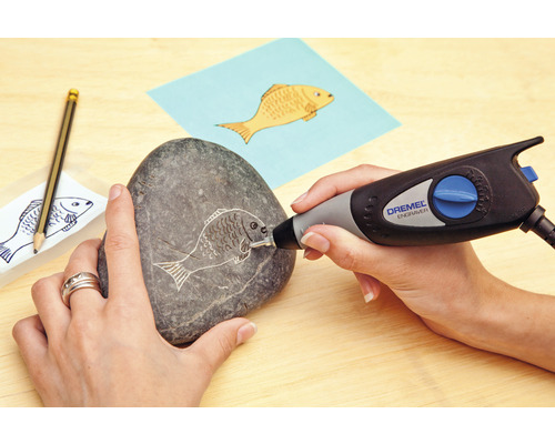 Une personne grave un motif de poisson dans une pierre avec un outil de gravure Dremel.