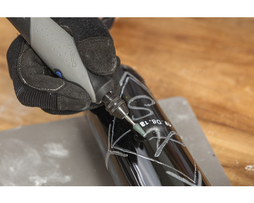 Une personne grave une bouteille sombre avec un outil Dremel.