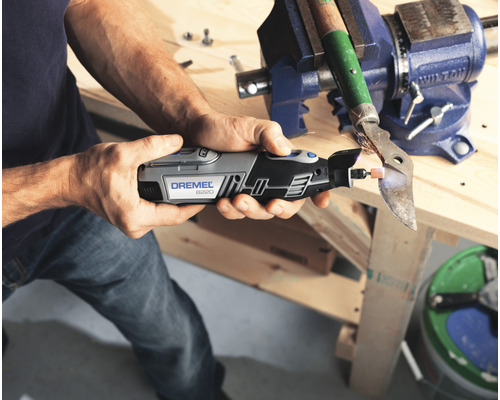 Un homme meule du métal avec un outil multifonction Dremel, fixé dans un étau