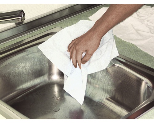 Une main essuie un évier en acier inoxydable avec un chiffon de nettoyage.