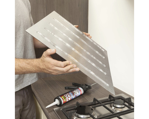 Protection anti-éclaboussures en acier inoxydable avec application d''adhésif, présentée avec un pistolet à colle sur une cuisinière.