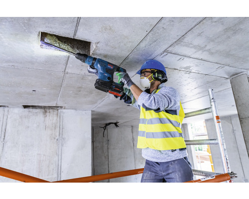 Ein Bauarbeiter bohrt mit einem Bohrhammer ein Loch in eine Betondecke.