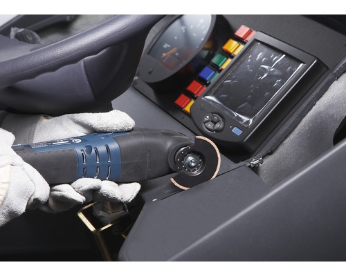 Bediener mit Schutzhandschuhen verwendet ein Multifunktionswerkzeug zum Schneiden eines Materials auf einer Baustelle