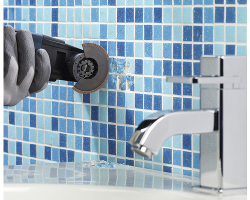 Ein Arbeiter mit Handschuhen entfernt Fliesen mit einem Multifunktionswerkzeug in einem Badezimmer