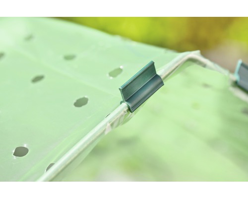 Nahaufnahme einer perforierten Folie, die mit Clips an einem Gewächshausrahmen befestigt ist.