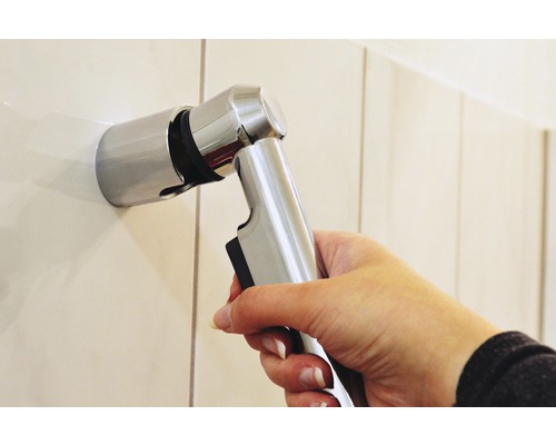Hand hält Bidet-Dusche aus Metall an Wandhalterung